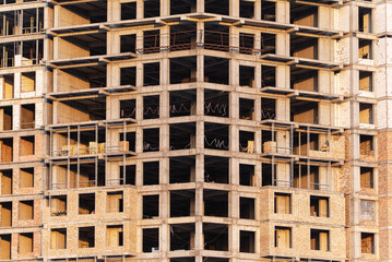 A detailed close-up shot of a modern residential or commercial building under construction. The concrete skeleton and exposed brick walls form a symmetrical grid of windows and structural elements.