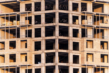 A detailed close-up shot of a modern residential or commercial building under construction. The concrete skeleton and exposed brick walls form a symmetrical grid of windows and structural elements.