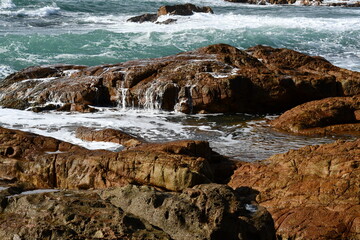 Reddish-organge rock formations in the intertidal zone creating tide pools near Australias Southeastern coastlines