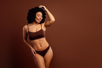 Fototapeta premium Charming young woman posing in brown underwear against a matching background portraying beauty and empowerment
