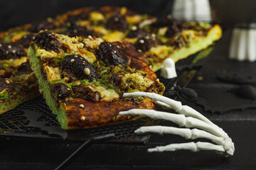 Spooky homemade pizza with green dough, mushroom skulls, and melted cheese. Halloween dark food