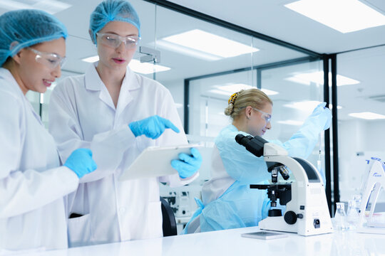 A pharmaceutical Quality Control QC team ensures GxP compliance. Two scientists review an electronic batch record on a tablet while a third performs a required analytical test.