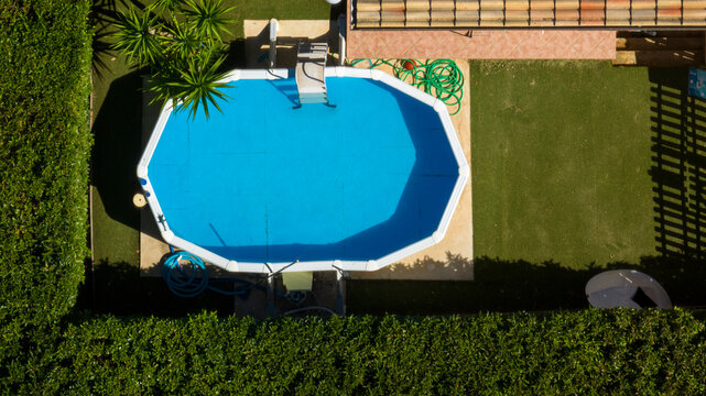 Aerial view of an octagonal inflatable pool. The pool is located in an empty garden. Surrounded by green grass.