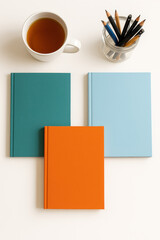 Flat lay arrangement with colorful notebooks in teal orange and light blue on white background next to cup of tea and jar of pencils with copy space for productivity and creative planning concept