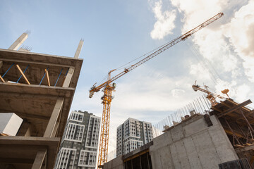 Construction site featuring cranes and rising buildings under a blue sky with clouds in an urban...