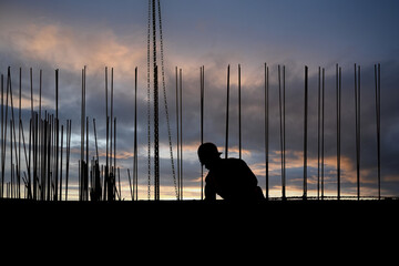 Construction worker silhouetted against a colorful sunset sky on a building site in the late evening
