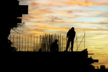 Construction workers building structure at dusk with colorful sky in background