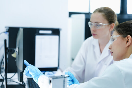 A pharmaceutical Quality Control QC team ensures GxP compliance. Two scientists review an electronic batch record on a tablet while a third performs a required analytical test.