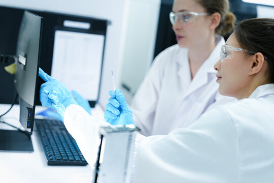 A pharmaceutical Quality Control QC team ensures GxP compliance. Two scientists review an electronic batch record on a tablet while a third performs a required analytical test.
