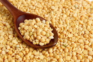 A wooden spoon with dry yellow peas lies on the surface.
