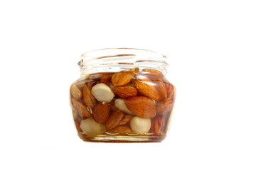 There is a glass jar with honey and nuts on a white background.	