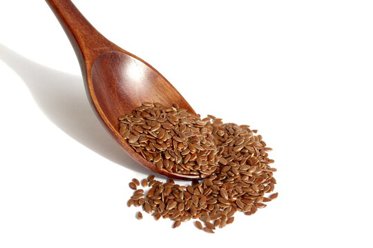 On a white background lies a wooden spoon with flax seeds.	