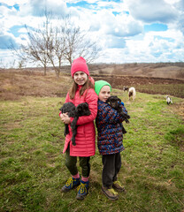Joyful boy and smiling girl holding black goats on the farm. Rural lifestyle, childhood and animal care in the countryside. Happy childhood.