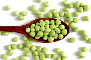 On a white background lies a wooden spoon with fresh green peas.	