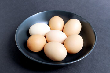 On a black background, there are chicken eggs in a black plate.	