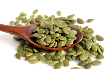 On a white background lies a wooden spoon with peeled pumpkin seeds.