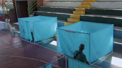 View of blue fabric booths labeled medicine and psychology inside a gymnasium during a free healthcare campaign in a Colombian rural community.