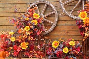Rustic Autumn Floral Decoration wood wall with Wagon Wheel and Sunflower. Fall Season Display Featuring Artificial Flowers background. Harvest Holiday Arrangement with Wooden Barn Siding and Wreath