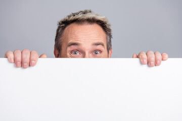 Confident mature man holding a blank whiteboard with a curious and engaging expression against a neutral background