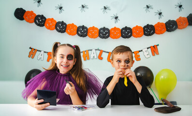 Two kids getting ready for Halloween. One girl applies makeup while boy inflates balloon.