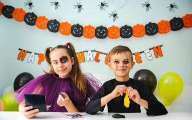 Two kids getting ready for Halloween. One girl applies makeup while boy inflates balloon.