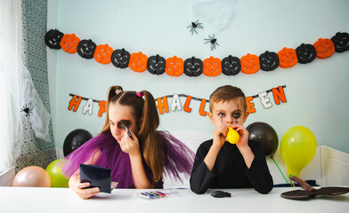 Two kids getting ready for Halloween. One girl applies makeup while boy inflates balloon.
