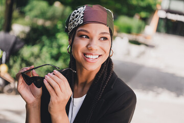 playful stylish woman smiles in sunny outdoor city park wearing headscarf and sunglass for travel...