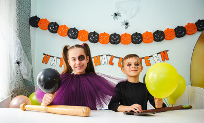 Two kids getting ready for Halloween. One girl applies makeup while boy inflates balloon.