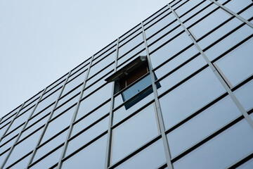 Low angle view of glass facade of modern office building with one open window against sky. Concept...