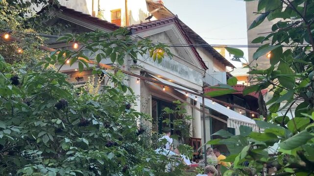 A low-angle shot captures the upper facade of an outdoor cafe in a Lviv courtyard, featuring a white triangular roof, string lights, and lush green foliage obscuring the lower half