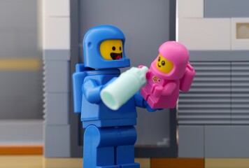 Obraz premium Tambov, Russian Federation - June 07, 2025 Lego astronaut minifigure feeding a baby cosmonaut minifigure using bottle.