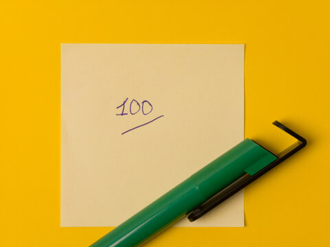 Perfect score of 100 handwritten on a yellow sticky note