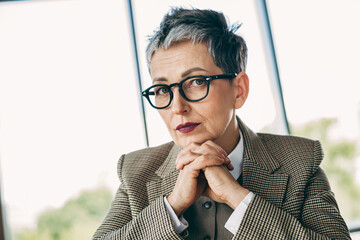 Confident mature businesswoman with stylish glasses and formalwear sitting in office, exuding professionalism and authority