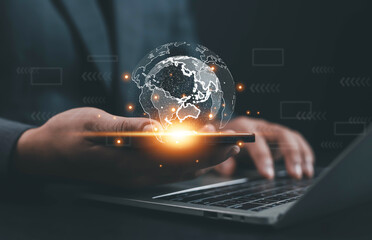 Businessman using smartphone and laptop with glowing digital globe hologram, representing global network connection, data innovation, technology communication, transformation for modern business.