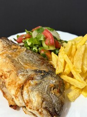 A close-up shot of fried potatoes, fried fish, and a salad with fresh vegetables and herbs. Cooking delicious food at home.