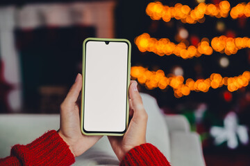 Funny cozy holiday moment a woman in a red sweater holds a smartphone in front of a lit Christmas...