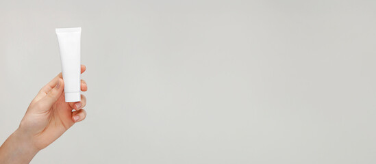 Female hand holding a tube of cream. Woman's hand showing cream tube. Cosmetic product branding mockup. Daily skincare and face care routine. Cosmetic product mock up, template, close up. Web banner