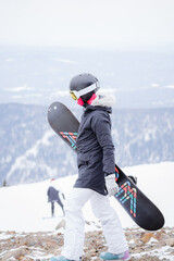 a girl with a snowboard in her hands walks forward along the slope