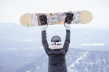 ski resort, raised a snowboard over her head at the top of the mountain
