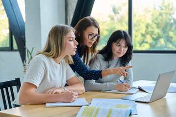 Two university student girls with female teacher mentor study while sitting at desk