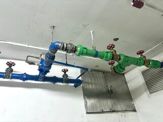 Industrial overhead piping system with bright blue metal and green plastic pipes connected by...