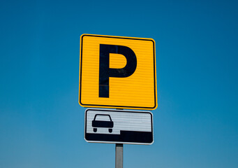 Yellow parking sign with letter P and car symbol against clear blue sky on a sunny day