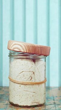 Close-up of wheat sourdough levito madre rising in a glass jar during time-lapse, expanding until the dough pushes up the wooden lid from inside due to fermentation pressure