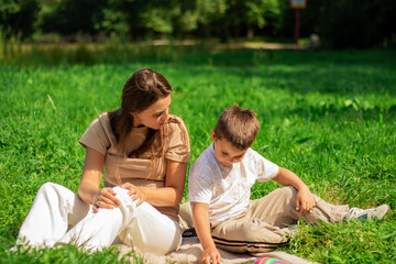Fototapeta premium Mom and her boy kid spending time together on nature and reading interesting book about dinosaurs. Quality time with child.
