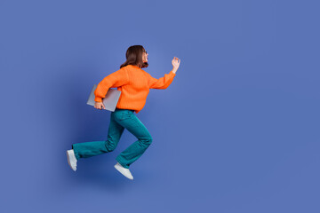 Energetic young woman in vibrant orange sweater running on blue background, portraying dynamic...
