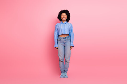 Fototapeta Smiling young woman wearing stylish casual clothing standing confidently against a vibrant pink background in studio setting