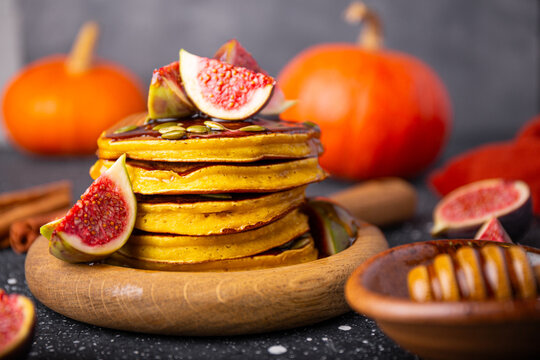 Stack of pumpkin pancakes with honey, pumpkin seeds and figs on a dark background. Concept of cozy homemade autumn food. Front view