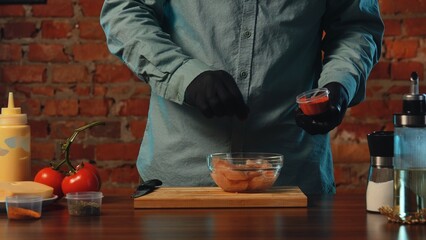 A chef seasoning raw chicken with spices. Ingredients include tomatoes, cheese, and condiments on a...