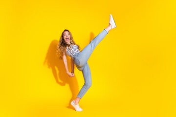 Cheerful young woman strikes an energetic pose wearing casual outfit against a vibrant yellow...