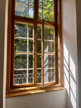 An aesthetic photo of the sunlight streaming through a classic wooden window looking out to lush greenery on a sunny day in the city of Budapest.
